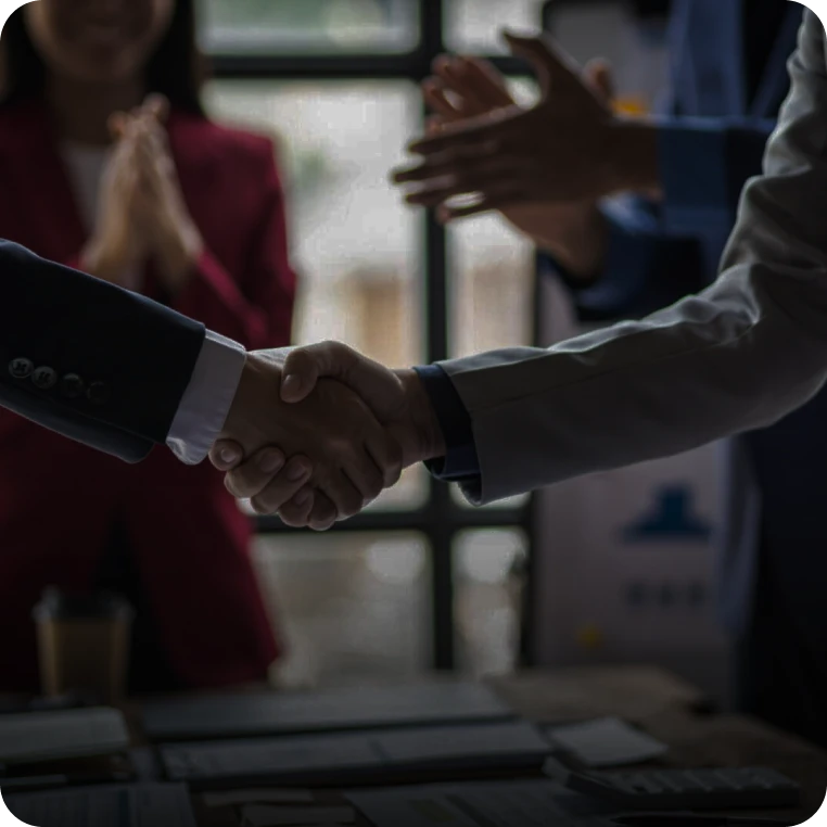 Handshake agreement with applauding colleagues nearby.
