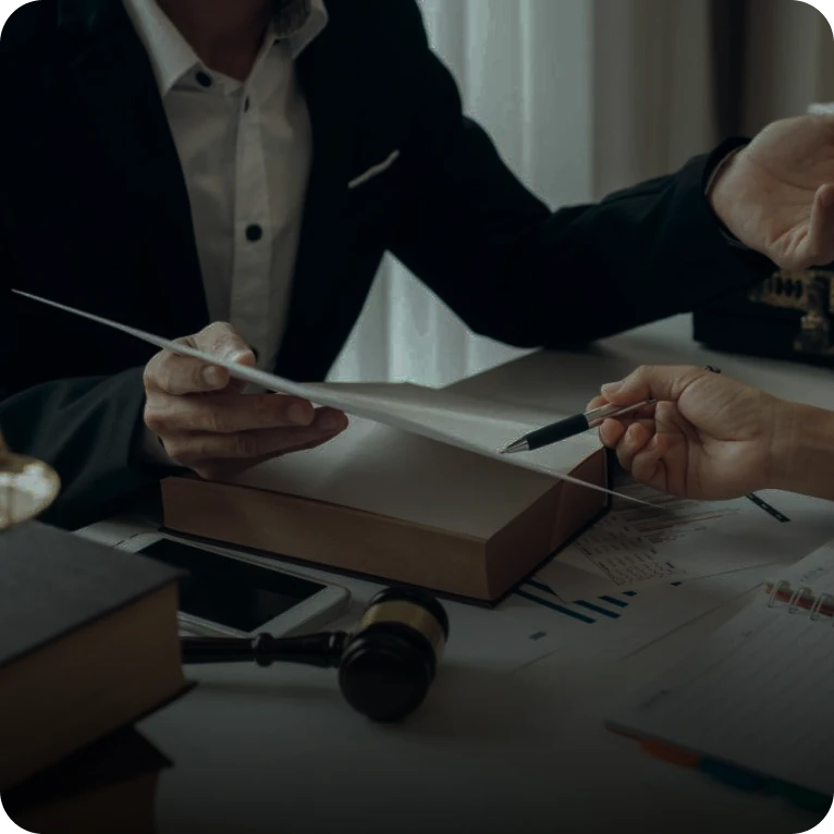 Hands exchanging pen over legal documents.